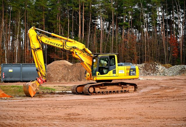 Excavator on a cleared dirt site at a forest edge